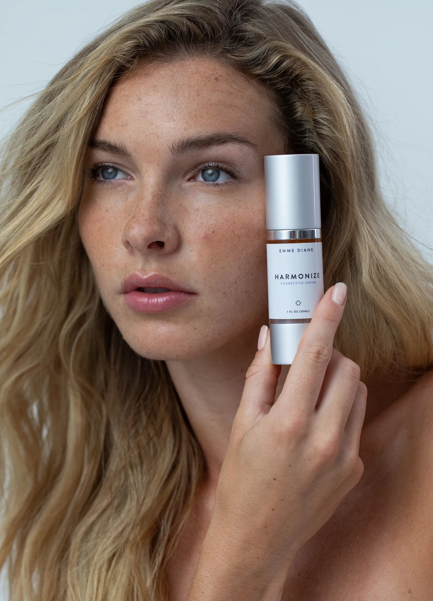 A woman holding Harmonize Corrective Serum beside her face.